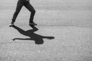 A person poses playfully on a street, casting an intriguing shadow on pavement photo