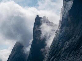 Great mountains in the fog. Low clouds and dark peaks of the mountains. Atmospheric surreal landscape with dark rocky mountain top in low clouds in cloudy sky. White low cloud on high pinnacle. photo