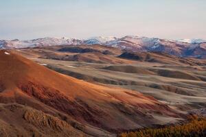 Unusual texture of the mountains, there is snow in the veins of the rock, the surface of the plateau is heated by the sun. Amazing red mountain plateau at sunset is lightly sprinkled with snow. photo