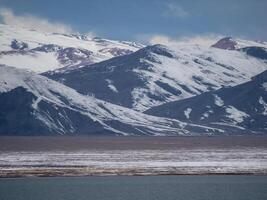 Dramatic landscape with snowy mountaintop in low cloudy sky. White snow on black rocks in low clouds. Awesome view to snow mountain peak in clouds. Lake with mountain, landscapes of Mongolia. photo