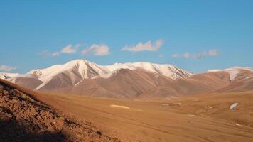 Wide panoramic view of bright autumn mountain steppe landscape. Awesome alpine view from pass to mountain valley in sunlight and great mountain silhouettes on horizon with white clouds on blue sky. photo