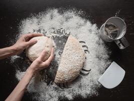Baker's hand holds the raw yeast-free dough on a dark background. White bread texture. Mankind oldest staple foods. photo