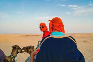 Tourists in the Sahara desert on camels. The entertainment of tourists. photo