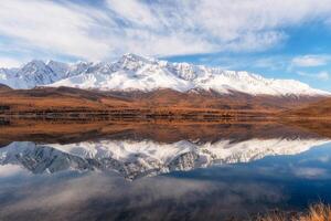 Beautiful autumn mountain lake and mountains. Reflection of snowy peaks and red coniferous taiga on the surface of a mountain lake. Russia. Altai Republic. Panoramic view. photo