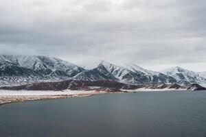 Snow-covered winter pastel colors landscape. View of the dark lake and snow hills. Cold winter weather. Harsh climate background in Mongolia. photo