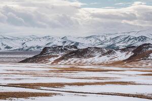 Pastel colors with the snow covered mountains in the distance. Scenic minimalist landscape with rocks in pastel tones. Snowy pasture scenery in winter. Mongolia landscapes. photo