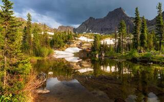 Taiga summer landscape. The purest mountain lake in the forest. Reflection of trees in the water. Sunny afternoon on the shore of a mountain lake, the remnants of snow on the slopes are melting. photo