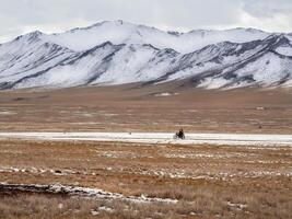 Beautiful Mongolian winter landscape snow mountain with a small figure of a ride on a black motorcycle through a wide snow-covered valley against the backdrop of high mountains. photo