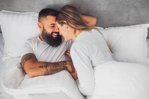 Happy loving couple is lying in bed in the morning. They are relaxing and smiling. photo