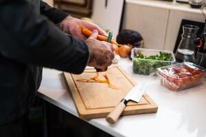Close up of professional chef preparing ingredients for vegetarian meal in restaurant's kitchen. He is scraping carrot. photo