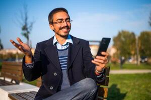 Businessman using mobile phone while sitting on a bench in the park photo