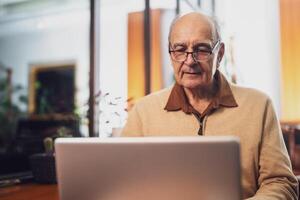Senior man in casual clothing with eyeglasses using laptop while enjoying sitting in the city cafe. photo