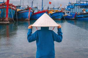 A child traveler in a traditional Vietnamese hat, inspecting traditional wooden boats in the port of Da Nang. photo