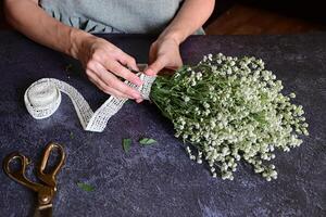 The photograph provides a close-up view of hands tying a white lace ribbon around a bouquet of delicate white flowers. photo