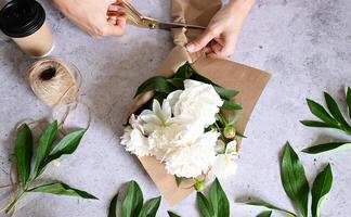 The image shows a person trimming the stems of a bouquet of white flowers, likely peonies. photo