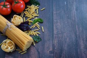 This photograph sets the stage for a pasta meal with ingredients like a bundle of spaghetti tied with a red ribbon, ripe tomatoes, chunks of cheese, garlic, fresh basil, and other additions photo