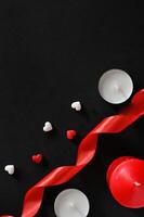 The picture shows a minimalist arrangement for a romantic occasion, using a white candle, a red candle, a red ribbon, and scattered heart-shaped candies in red and white, set against a plain photo