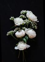 The image showcases an elegant floral arrangement of white peonies and smaller white filler flowers against a stark black background. photo