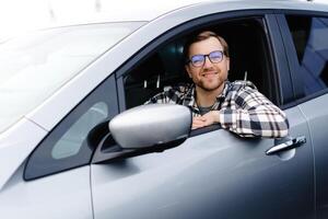 Man customer sitting in car salon and smiling, choosing auto and wanting to buy new automobile in showroom dealership store. Car sales concept. photo