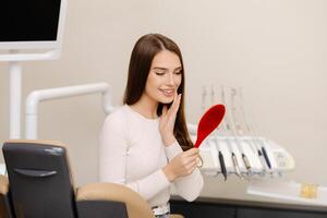 Pretty girl smiling while sitting in the dentist's chair, holding a mirror in her hands photo