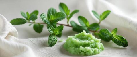Fresh mint leaves and green herbal scrub arranged on a soft fabric backgroundFresh mint leaves and green herbal scrub arranged on a soft fabric background. photo
