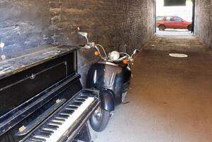 An old piano with a retro moped in the archway of the house on a sunny day. photo