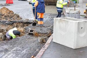 A group of road workers repair sewer storm hatches on a roadway on an autumn day. photo