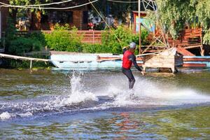 An athlete wakeboarder makes a sharp turn on the surface of the water at high speed, raising a pile of spray behind him. photo