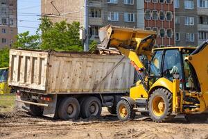 A tractor with a large bucket loads soil into the back of a large truck. photo
