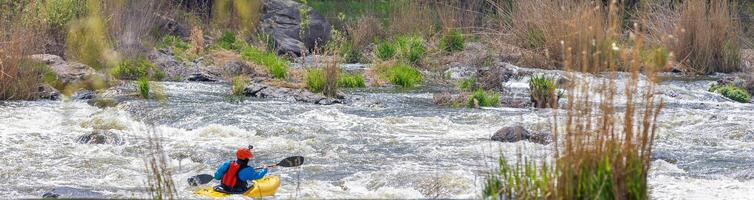 An athlete on a kayak overcomes a turbulent stream of water on the rocky rapids of the river. photo