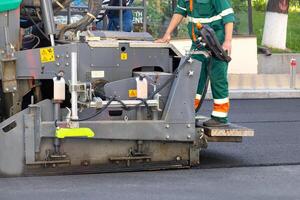 A fragment of the work of an industrial asphalt paver, an engineer stands on the footboard and controls the process. photo