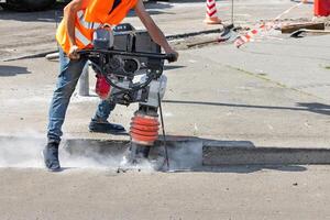 A construction worker is ramming a trench with a vibrating rammer at a construction site and kicking up a cloud of dust around him. photo