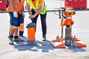 Road workers in reflective raincoats drill asphalt with a core drill. photo