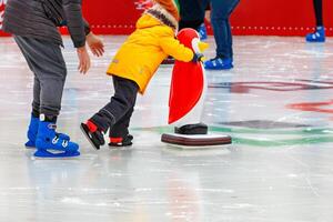 A child, accompanied by an adult, learns to skate on an ice rink, holding on to an assistant, a toy penguin. photo
