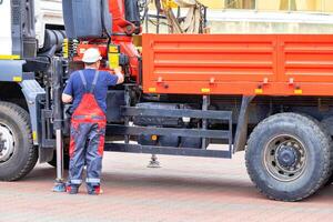 The driver of a truck with a hydraulic manipulator examines and adjusts the operation of the lifting mechanism. photo