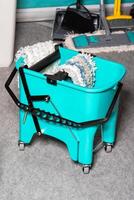 Turquoise bucket on wheels with an original rag wringing system on a gray background. Copy space. photo