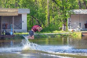 Wakeboarder leaps from the water, creating splashes under the bright sun in vibrant summer day of wakeboarding fun at the lakeside park. photo