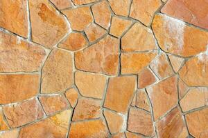 Natural stone wall with textured surface displaying rustic patterns, interlocking shapes, and warm earthy tones, architectural design concept. photo