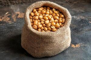Roasted peanuts filling a burlap sack on a dark background photo