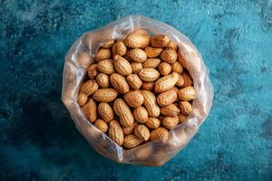 Peanuts in shell filling transparent plastic bag on rustic turquoise background photo