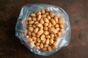 Plastic bag overflowing with shelled peanuts on dark background photo