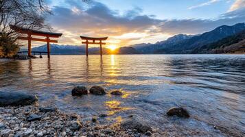 Iconic red torii gate at sunset over tranquil water with mountains photo