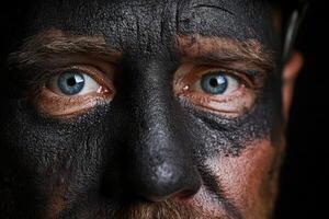 Miner with coal dust face gazes intensely into the camera during work photo