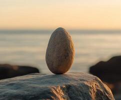 Natural stone egg balanced on a rock by the ocean at sunset photo