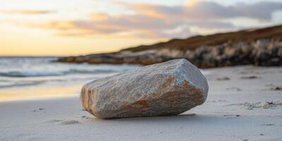 Natural stone on sandy beach during sunset by the ocean waves photo