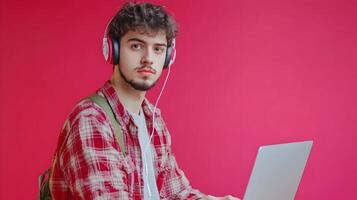 Portrait of a Focused Young Male Student Deeply Engaged in Academic Research and Studies,Using a Laptop Computer and Wearing Headphones on a Vibrant Colored Background. photo
