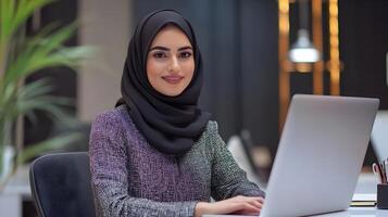 Portrait of a young,stylishly dressed Muslim woman wearing a hijab,working intently on a laptop computer at her desk in a contemporary office setting. photo