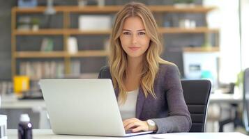 Portrait of a young,confident Caucasian female business executive sitting at a desk and using a laptop computer in a modern,professional office environment. She appears to be working on marketing. photo