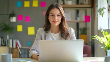 Portrait of a stylish and professional young Caucasian female manager sitting at a desk and using a laptop computer in a modern and well-equipped marketing agency office. She is focused on her work. photo