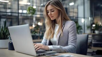 Portrait of a focused and determined young Caucasian female manager working intently on her laptop computer while seated at a desk in a contemporary corporate office environment. photo